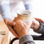 Elder being supported by professional caregiver by providing coffee